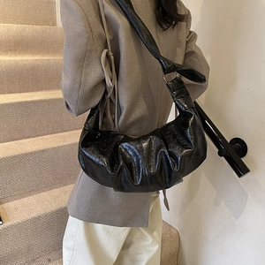 Black pleated faux leather croissant bag shown on model with chic beige blazer