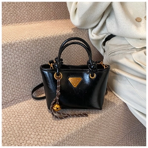 Détail du sac cabas en cuir noir brillant avec logo doré et charm en corde tressée