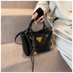 Détail d'un sac cabas en cuir verni noir avec logo doré et pendentif en corde tressée