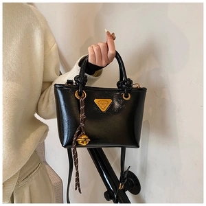 Détail du sac cabas en cuir brillant noir avec logo triangle doré et pompon chic