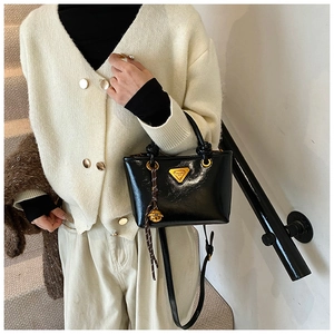 Gros plan d'un mini cabas en cuir verni noir avec logo triangle doré et accessoire