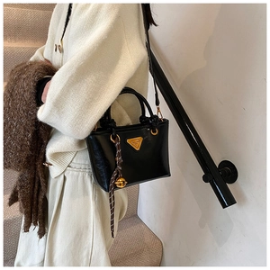 Détail d'un petit cabas en cuir verni noir brillant avec logo doré et poignée