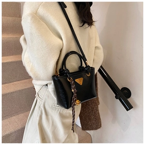 Détail du sac à main en cuir noir brillant avec plaque en métal et breloque décorative