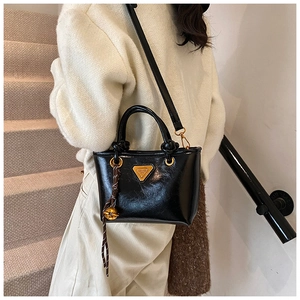 Détail d'un sac cabas en cuir verni noir avec logo doré et pendentif tressé