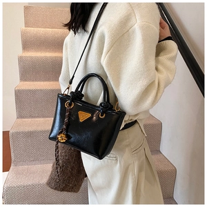 Détail du sac à main noir brillant avec logo triangle doré et décor de poignée nouée