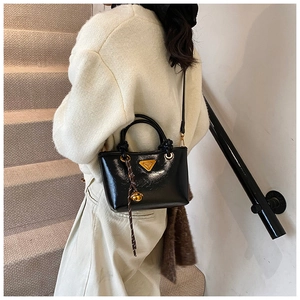 Détail du sac cabas en cuir verni noir avec triangle doré et pendentif en corde tressée