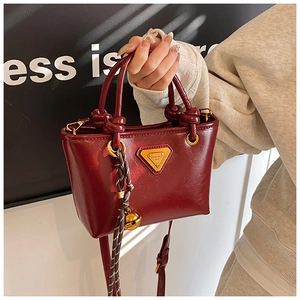 Détail d'un sac seau bordeaux avec texture plissée brillante et plaque dorée