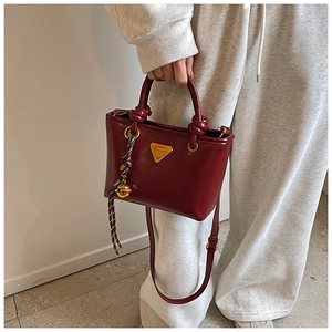 Détail du sac à main bordeaux brillant avec poignées rondes et breloque tissée