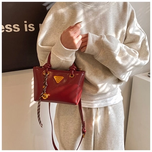 Détail d'un sac à main bordeaux en cuir avec logo doré et ruban tissé décoratif