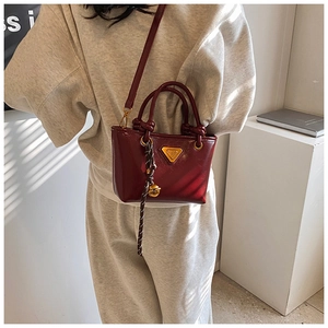 Détail du sac seau rouge en cuir avec logo doré et pompon porté par un mannequin
