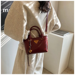 Détail d'un sac cabas bordeaux brillant avec logo doré et pendentif cloche tressé