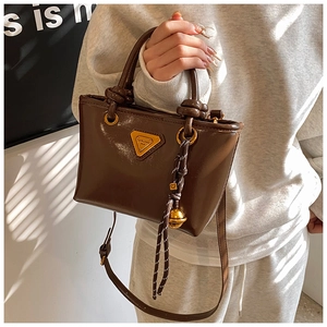 Détail du sac à main en cuir marron avec logo triangulaire doré et pendentif tressé