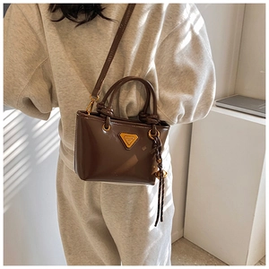 Gros plan du mini sac fourre-tout marron brillant avec logo métallique et breloque tissée