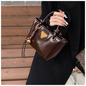 Détail du sac cabas brillant marron café avec logo triangle doré et breloque cloche