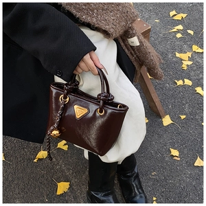Détail du mini cabas en cuir verni marron foncé avec logo doré et poignée nouée