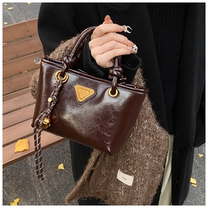 Détail du sac à main marron brillant avec poignée à nœud et logo triangulaire doré