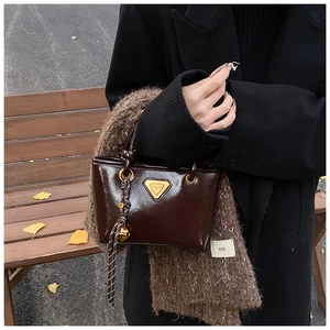 Détail du mini sac cabas en cuir verni marron foncé avec plaque dorée et breloque