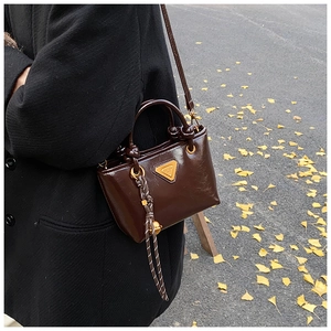 Détail d'un mini sac cabas en cuir verni marron foncé avec logo doré et bandoulière