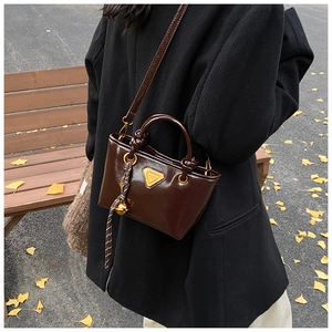 Détail d'un mini sac cabas en cuir verni marron foncé avec logo et breloques dorées