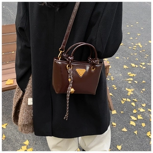 Vue détaillée d'un sac seau en cuir verni marron foncé brillant avec une tenue d'automne