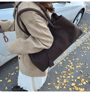 Detail of dark brown matte tote bag with long straps worn on shoulder with a beige coat