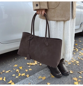 Close-up of large dark brown suede tote bag with double handles and a leaf charm
