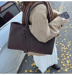 Detail of dark brown suede tote bag featuring a decorative long tassel and minimal design