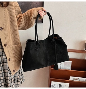 Close-up of black suede tote bag showing texture, vertical seams and side leather tag