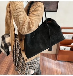 Close-up of a large black suede tote bag with leather straps on model's shoulder
