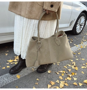 Detail of taupe suede tote bag with long handles and charm in an autumn street setting