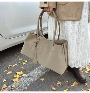 Close-up of khaki suede tote bag with decorative tag in a stylish outdoor setting
