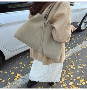 Close-up of a large suede tote bag in khaki with long strap detail in an autumn street setting