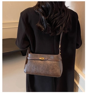 Dettaglio della borsa vintage in pelle marrone con fibbia dorata su cappotto nero