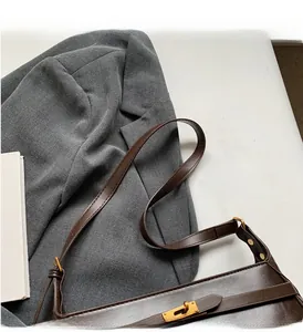 Dettaglio borsa a tracolla in pelle testa di moro con chiusura dorata su blazer grigio