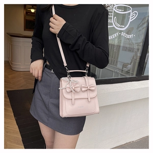 Gros plan du sac bandoulière en cuir rose clair avec nœuds et pendentif perle papillon