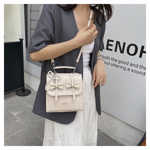 Détail du sac bandoulière crème avec nœuds, perles et logo FASHION gravé