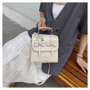 Détail du sac à dos blanc crème avec nœuds, pendentif cœur perlé et texte de mode