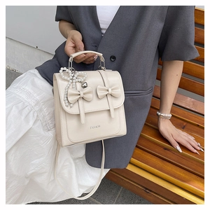 Détail du sac à main blanc cassé avec nœuds et pendentif cœur en perle