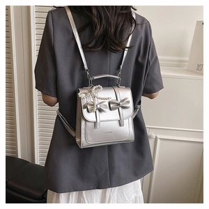 Détail du mini sac à dos argenté métallisé avec nœuds décoratifs et accessoire en perles