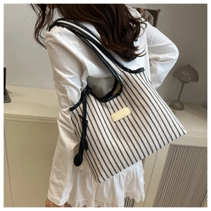 Detail of a large striped tote bag with leather tag and slim straps worn by a model