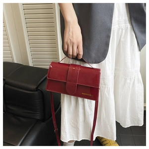 Detail of red glossy patent leather crossbody bag with gold lettering held by a model