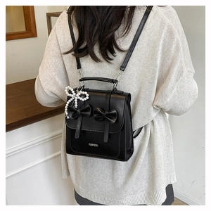Détail d'un sac à dos noir avec deux nœuds 3D et un pendentif délicat en perles