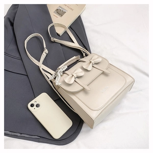 Détail du sac beige à nœud avec breloque perle et impression de logo tendance