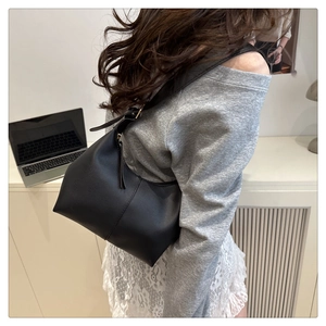 Close-up of minimalist black leather hobo shoulder bag styled in a modern office setting