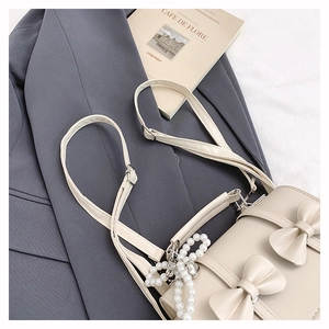 Détail du sac à dos beige avec nœuds et pendentif perle sur fond de tissu neutre