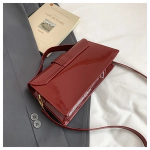 Detail of burgundy patent leather shoulder bag with gold hardware on a gray blazer