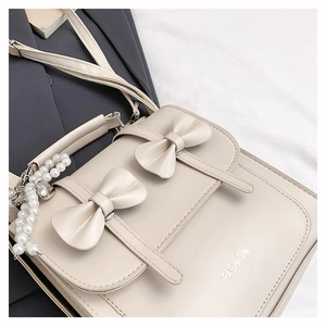 Détail du sac beige avec nœuds décoratifs, chaîne de perles et lettrage FASHION