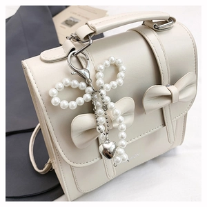 Détail du sac à main blanc cassé avec pendentif nœud en perles et breloque cœur