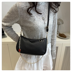 Detail der schwarzen Achseltasche mit Lychee-Muster und goldener Herz-Kette