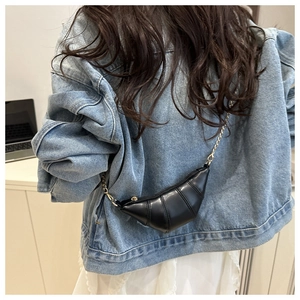 Détail d'un sac croissant noir avec bandoulière en chaîne dorée porté sur une veste en jean